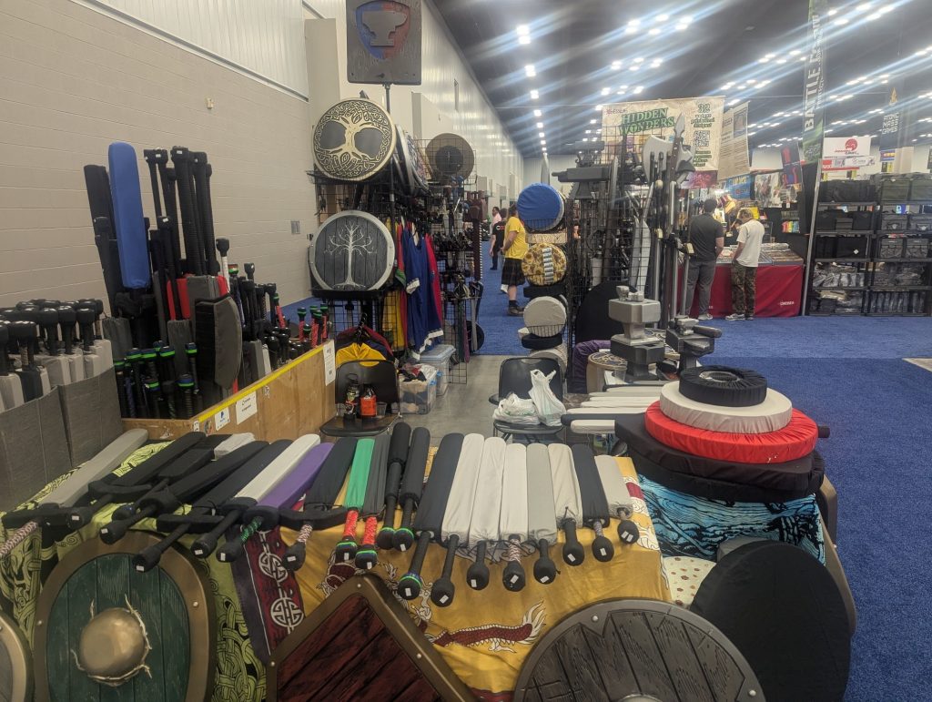 The Forged Foam booth at a convention, showcasing different types of LARP weapons and shields for sale.